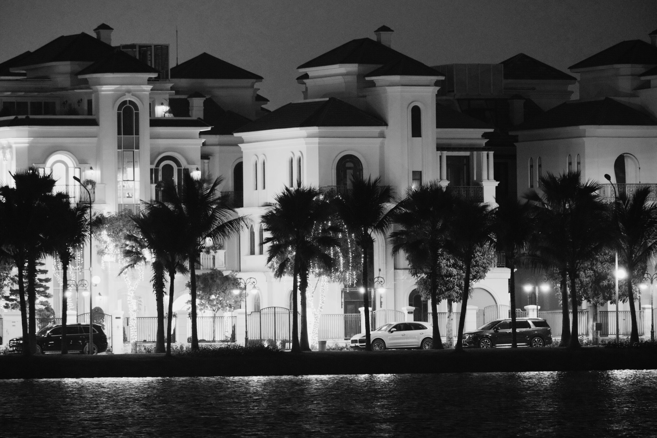 Luxury homes with palm-lined entrance at night